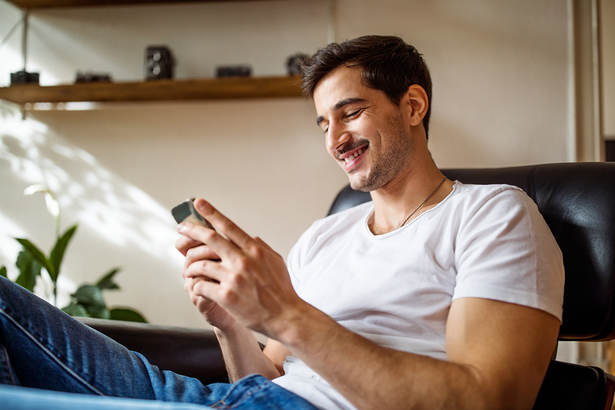 A man sitting in a chair and smiling at his phone